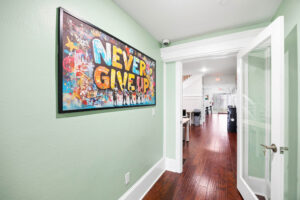Gallery hallway with green walls and a colorful "NEVER GIVE UP" artwork on a left wall.